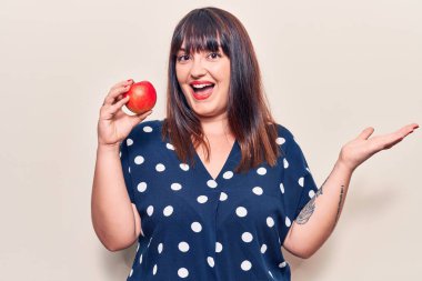 Kırmızı elma tutan genç ve cüsseli bir kadın başarıyı mutlu bir gülümsemeyle ve kazanan bir ifadeyle kutluyor. 