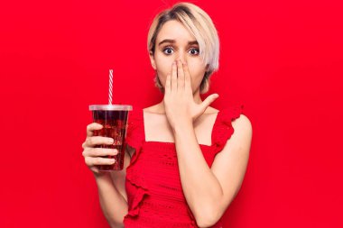Genç ve güzel sarışın bir kadın bir bardak kola içiyor. Ağzını eliyle kapatıyor. Şok geçiriyor ve hata yapmaktan korkuyor. şaşırmış ifade 