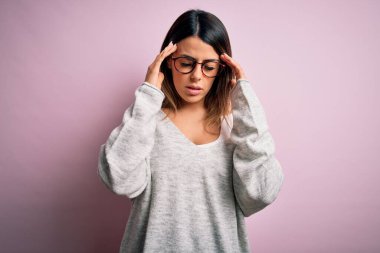 Genç, güzel, esmer bir kadın pembe arka planda rahat süveter ve gözlük takıyor. Stres yüzünden başının üstünde baş ağrısı var. Migren ağrısı..