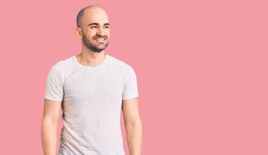 Gündelik tişört giyen genç yakışıklı adam yüzünde gülümsemeyle yan yana bakıyor, doğal bir ifade. Kendinden emin gülen. 