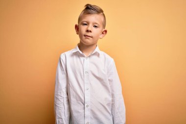 Mavi gözlü, sarı arka planda zarif beyaz gömlek giyen, yüzünde ciddi bir ifade olan küçük beyaz bir çocuk. Basit ve doğal bir şekilde kameraya bakıyorsun..