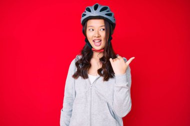 Bisiklet kaskı takan, gülümseyen, gülümseyen güzel Çinli kız başparmağıyla yan tarafa bakıyor ve işaret ediyor.. 