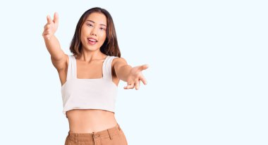 Gündelik giysiler giymiş genç, güzel Çinli bir kız kameraya bakıyor ve sarılmak için kollarını açmış gülümsüyor. Mutluluğu kucaklayan neşeli bir ifade.. 