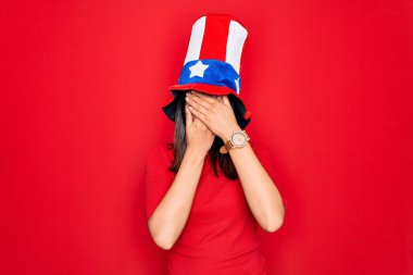 Amerika Birleşik Devletleri şapkası takan genç, güzel esmer kadın bağımsızlık gününü kutluyor gözlerini ve ağzını kapıyor, şaşırmış ve şok olmuş. Duygularını gizliyor.