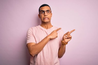 Yakışıklı Afro-Amerikalı adam pembe arka planda günlük tişört ve gözlük takıyor. Endişeli ve gergin, endişeli ve şaşırmış bir ifadeye işaret ediyor.