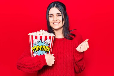 Patlamış mısır yiyen genç ve güzel bir kız gururla bağırıyor, zaferi kutluyor ve başarıyı kollarını kaldırarak kutluyor. 