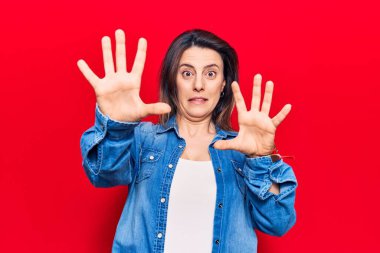 Gündelik kıyafetler giyen genç ve güzel bir kadın korku ifadesi yüzünden korkmuş ve dehşete düşmüş. El hareketlerini durdur, şok içinde bağır. panik konsepti. 