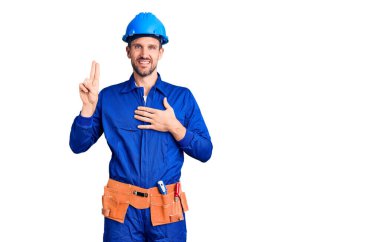 Genç, yakışıklı, işçi üniforması giyen, kasklı, gülümseyen, elleri göğsünde ve parmakları havada yemin eden, sadakat yemini eden bir adam. 