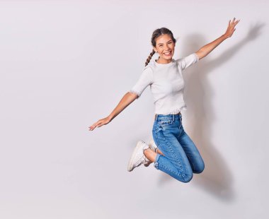 Saçları örgülü, sıradan kıyafetler giyen, mutlu gülümseyen genç ve güzel bir kadın. Yüzünde ve kollarında tebessümle atlayan izole beyaz arka planda açılan