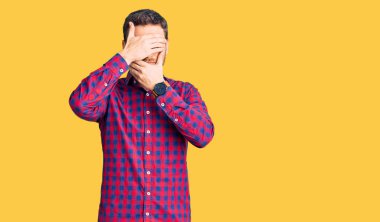 Ayılı yakışıklı genç adam, gündelik gömlek giyiyor gözleri ve ağzı elleri kapalı, şaşırmış ve şok olmuş. duygu gizleme 