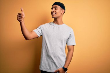 Yakışıklı Afro-Amerikan sporcu sarı arka planda spor giysisi giyiyor. Gururlu, gülümseyen, baş parmaklarını kaldıran bir jest yapıyor.