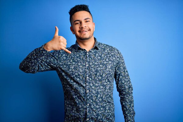 Young handsome man wearing casual shirt standing over isolated blue background smiling doing phone gesture with hand and fingers like talking on the telephone. Communicating concepts.