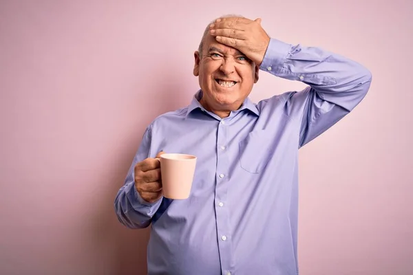 Middle age handsome hoary man drinking mug of coffee over isolated pink background stressed with hand on head, shocked with shame and surprise face, angry and frustrated. Fear and upset for mistake.