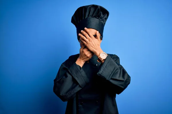 年轻的非洲女厨师身穿炊具制服 头戴蓝色背景的帽子 双手捂住眼睛和嘴 感到惊讶和震惊 隐藏感情 — 图库照片