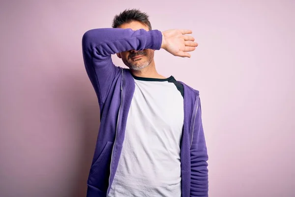 年轻英俊的男子穿着紫色运动衫和眼镜 站在粉色的背景上 用胳膊蒙住眼睛 看起来严肃而忧郁 目光短浅 躲藏和拒绝的概念 — 图库照片