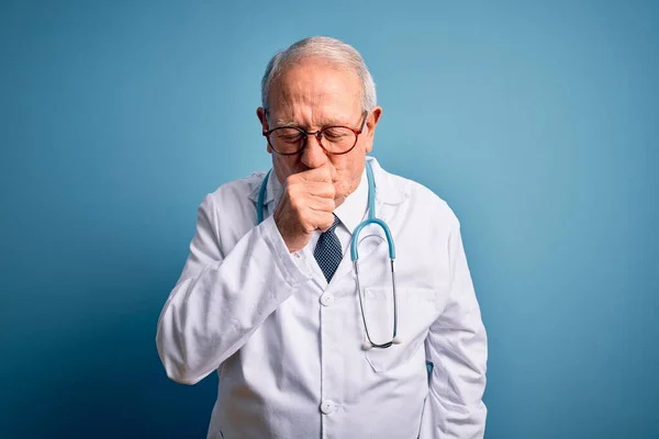 青い背景感の上に聴診器と医療用のコートを身に着けているシニアグレーの髪の医者の男は具合が悪く 風邪や気管支炎の症状として咳 ヘルスケアの概念 — ストック写真