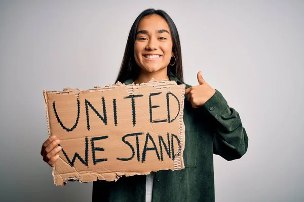 Young beautiful activist asian woman asking unity holding banner with united stand message with surprise face pointing finger to himself