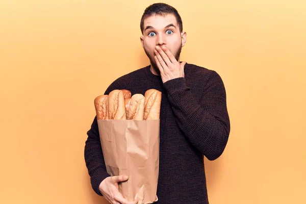 Joven Hombre Guapo Sosteniendo Bolsa Papel Con Pan Cubriendo Boca —  Fotos de Stock