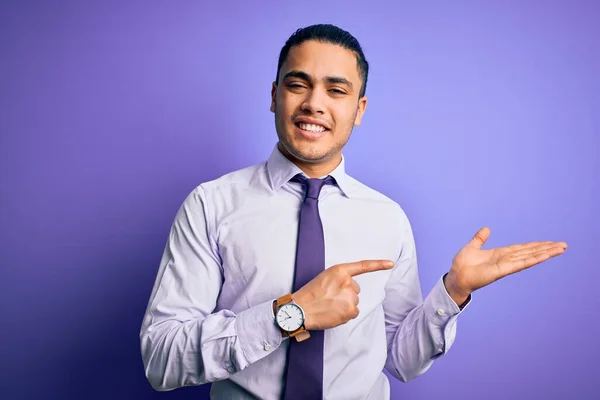 手で提示し 指で指している間若いブラジルのビジネスマンは カメラに驚いて笑顔孤立した紫色の背景の上に立ってエレガントなネクタイを身に着けています — ストック写真