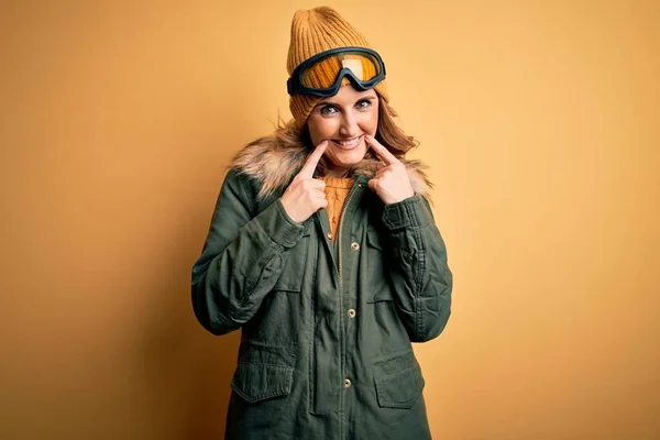 中年美丽的金发滑雪者女人穿着雪地运动鞋和滑雪护目镜 张开嘴微笑 手指指尖 笑容可亲 — 图库照片
