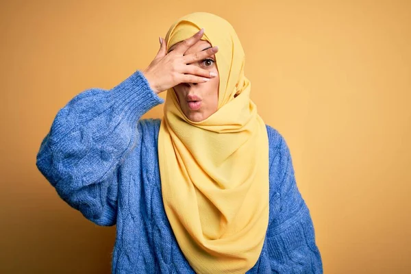 若いです美しいですブルネットムスリム女性身に着けていますArab Hijab上の隔離された黄色の背景Peekでショックカバー顔と目で手 を通して見る指で恥ずかしい表現 — ストック写真