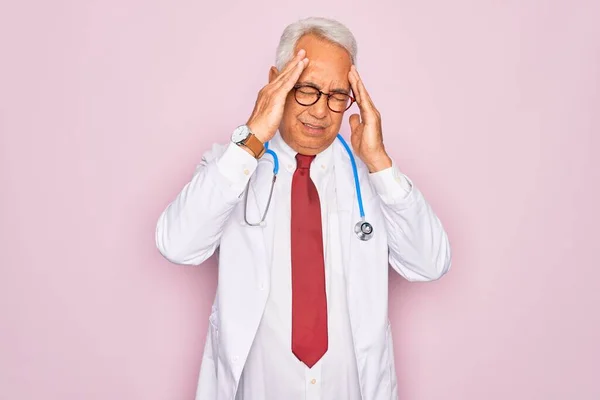 ストレスが原因で頭痛に手で聴診器やプロの医療コートを身に着けている中世のシニア白髪の医師の男 片頭痛に苦しむ — ストック写真