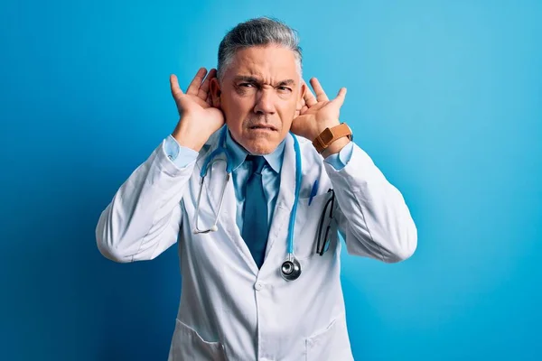 中年英俊的白发苍苍的医生 身穿外套 头戴蓝色听诊器 竭力想听到两只手按在耳朵上的手势 好奇地闲聊着 听力问题 — 图库照片
