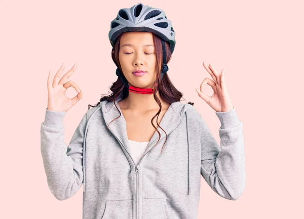 Young beautiful chinese girl wearing bike helmet relax and smiling with eyes closed doing meditation gesture with fingers. yoga concept.