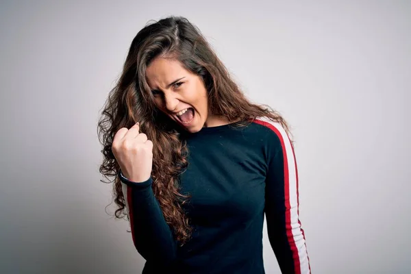 Young beautiful woman with curly hair wearing casual sweater over isolated white background angry and mad raising fist frustrated and furious while shouting with anger. Rage and aggressive concept.