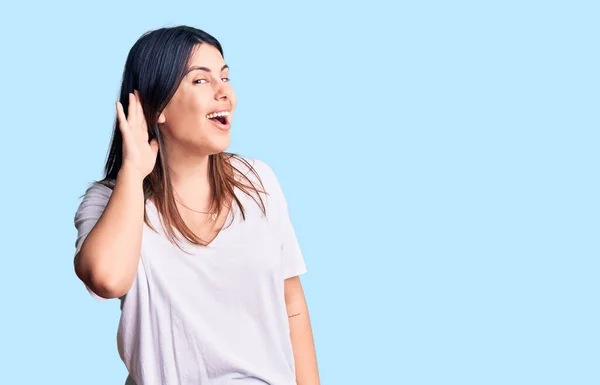 噂やゴシップに耳を傾ける耳の上に手で笑顔カジュアルなTシャツを着て若い美しいブルネットの女性 聴覚障害の概念 — ストック写真