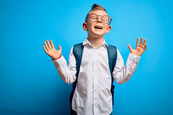 年轻的小高加索学生 戴着聪明的眼镜 背着蓝色背景的书包 带着兴奋的高举双臂和紧闭的眼睛庆祝着成功的疯狂和疯狂 赢的概念 — 图库照片