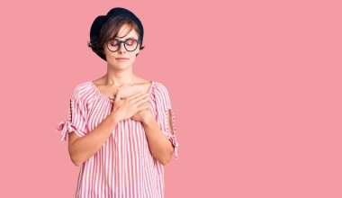 Kısa saçlı, günlük kıyafetler giyen, gözlüklü, göğsünde elleri kapalı, yüzünde minnet ifadesi olan güzel bir kadın. sağlık kavramı. 