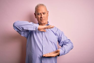 Orta yaşlı, beyaz gömlekli yakışıklı adam pembe arka planda dikiliyor. Elleri büyük ve büyük boy işareti gösteriyor. Ölçüm sembolü. Kameraya bakıp gülümsüyor. Ölçüm konsepti.