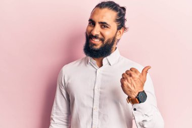 Gündelik kıyafetler giyen, gülen yüzlü genç bir Arap başparmağıyla yan tarafa bakıyor ve işaret ediyor.. 
