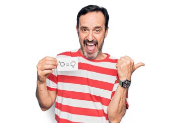 Orta yaşlı bir adam, kadın ve erkek eşit haklara sahip kağıtlar istiyor. Başparmağıyla yan tarafı işaret ediyor. Ağzı açık mutlu bir şekilde gülümsüyor.