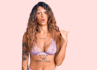 Dövmeli, iç çamaşırlı genç İspanyol kadın elini yana uzatarak şaşırdı, ağzı açık şaşkın bir ifadeyle.. 