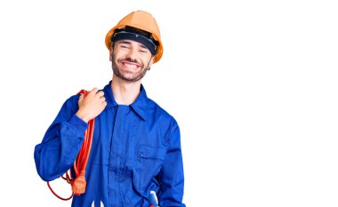 Genç İspanyol adam elektrokrat üniforması giyiyor. Kablo tutuyor. Olumlu ve mutlu görünüyor. 