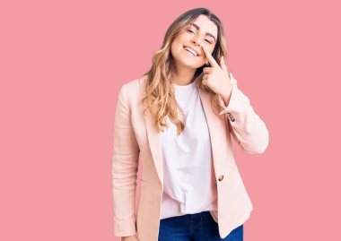 İş kıyafetleri giymiş genç beyaz bir kadın el ve burnu işaret ederek neşeli bir şekilde gülümsüyor. güzellik konsepti 