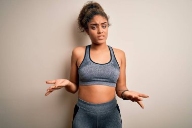 Genç Afrikalı Amerikalı sporcu kadın spor giysisi giyiyor beyaz arka planda bilgisiz ve kolları açık, hiçbir fikri yok..