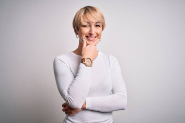 Genç, sarışın, modern kısa saçlı bir kadın izole edilmiş arka planda duruyor. Kameraya bakıyor, kollarını kavuşturup, çenesini kaldırarak gülümsüyor. Olumlu düşünüyorum..