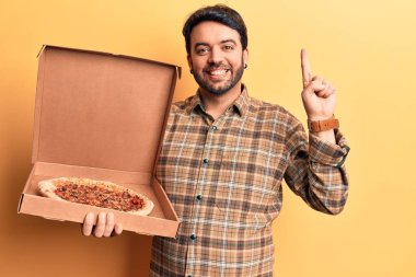 İspanyol asıllı genç adam elinde pizza kutusuyla bir fikir ya da soruyla gülümsüyor ve mutlu bir yüzle işaret ediyor. 