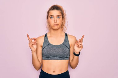Mavi gözlü genç sarışın spor kadın spor kıyafetleri giyiyor üzgün ve üzgün görünüyor, parmaklarıyla yön gösteriyor, mutsuz ve depresif..