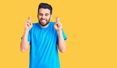 Sakallı, sıradan bir tişört giyen, umut dolu ve gözleri kapalı bir şekilde gülümseyerek el hareketi yapan genç yakışıklı bir adam. Şans ve batıl inançlar. 