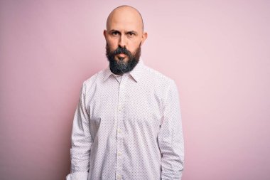 Soyutlanmış pembe arka planda zarif gömlek giyen sakallı yakışıklı kel adam depresif ve endişeli, sinirli ve korkmuş. Üzücü ifade.