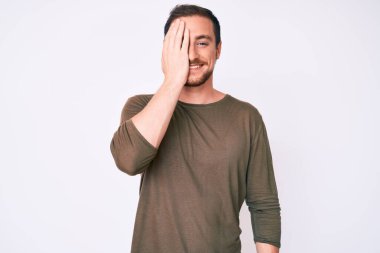 Gündelik kıyafetler giyen genç yakışıklı adam bir gözünü eliyle kapatıyor, yüzünde kendine güvenen bir gülümseme ve şaşırtıcı bir duygu var.. 