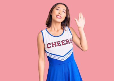 Genç, güzel Çinli kız ponpon kız üniforması giyiyor. Merhaba diyor. Mutlu ve gülümsüyor. 