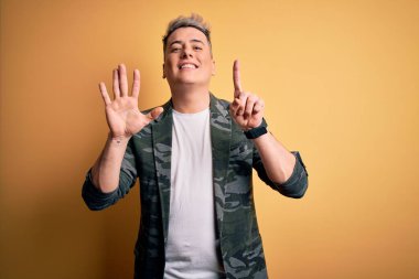 Sarı arka planda duran iş ceketi giyen yakışıklı ve modern bir adam altı numaralı parmaklarıyla gülümseyerek kendinden emin ve mutlu bir şekilde onu işaret ediyor..