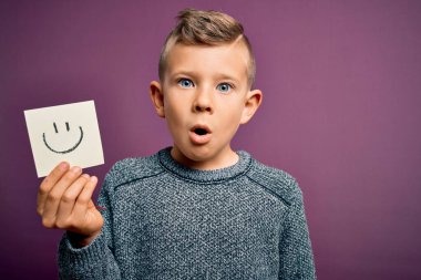 Küçük beyaz bir çocuk kağıtta gülen yüzünü gösteriyor. Mutlu bir mesaj gibi. Şaşırmış bir yüzle korkmuş ve korku ifadesinden heyecanlanmış.