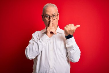 Orta yaşlı yakışıklı, beyaz gömlekli ve kırmızı arka planda gözlüklü bir adam sessiz olmak istiyor. Sessizlik ve gizli konsept.