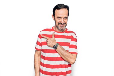 Orta yaşlı, çizgili tişört giyen yakışıklı adam izole edilmiş beyaz arka planda dikiliyor. Gülümsüyor, eli ve parmağı yana doğru uzanıyor.